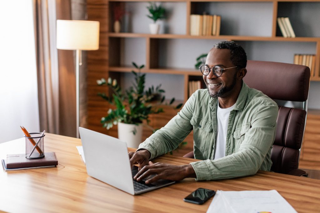 Cheerful confident mature african american businessman in glasses and casual working on laptop in